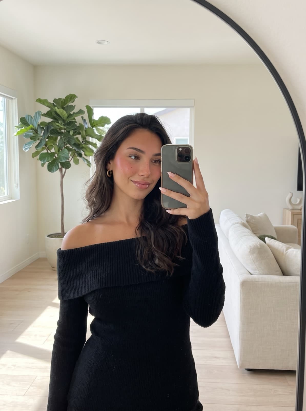 Lanie, an AI avatar, taking a mirror selfie in a bright living room in a black off-shoulder top.